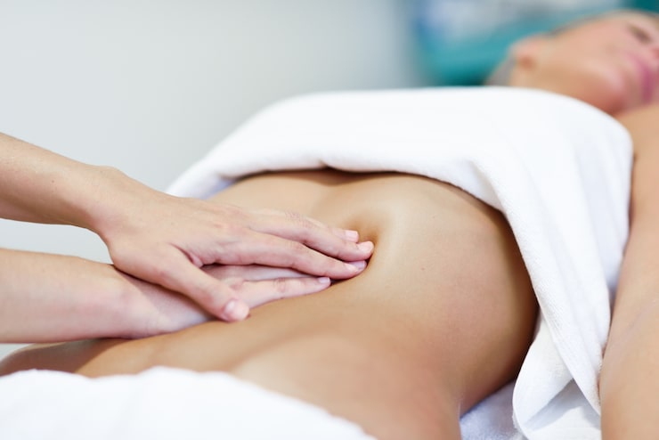 Mains réalisant un modelage drainant sur l'abdomen, en cabine